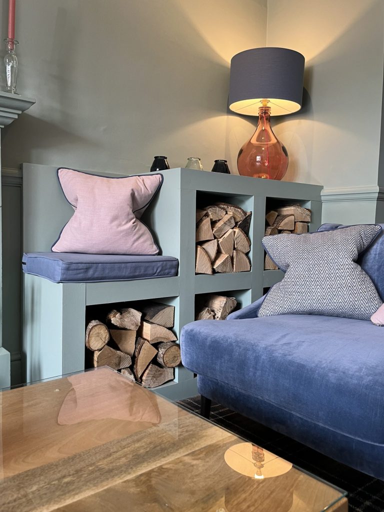 Snug with a built-in log store and blue velvet sofa, designed by Pip Interior Designs in York