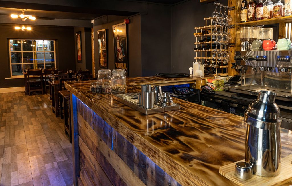 Charred and lacquered timber bar top looking through to the restaurant, the Log Room at the Feversham Arms, Helmsley