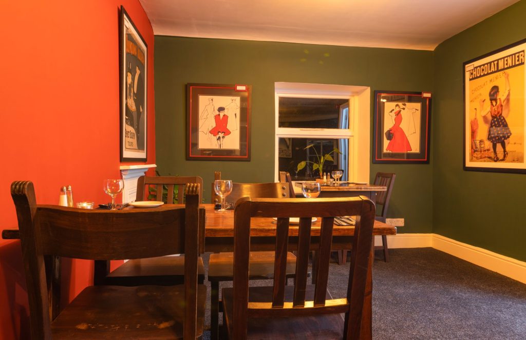 Side dining room with burnt orange and olive green walls and framed prints, the Log Room at the Feversham Arms, Helmsley