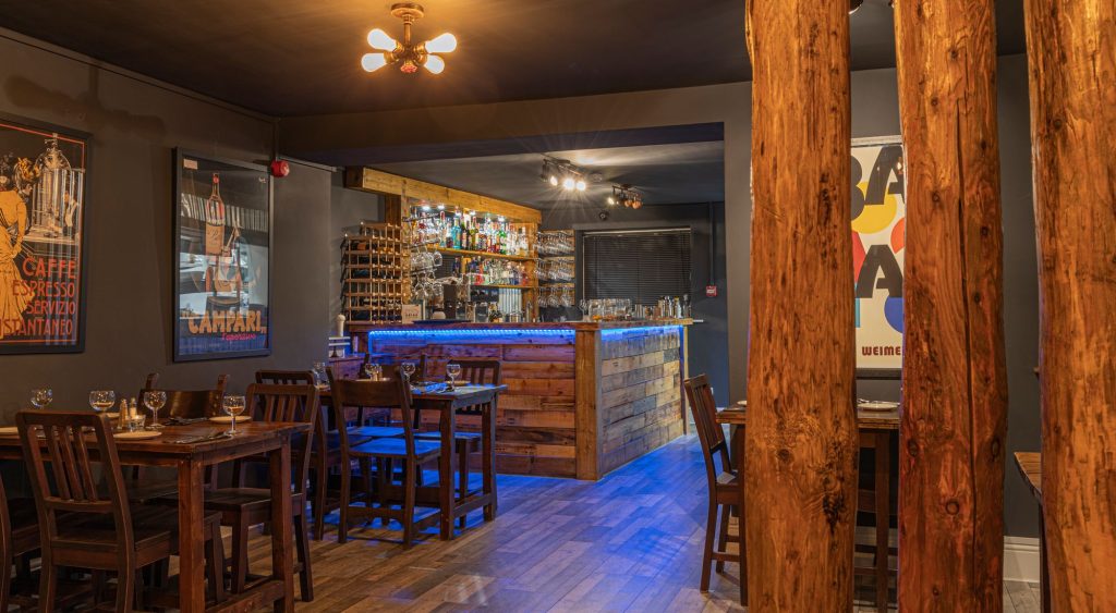 Restaurant interior with dark walls, reclaimed timber columns and a blue-lit bar, the Log Room at the Feversham Arms, Helmsley