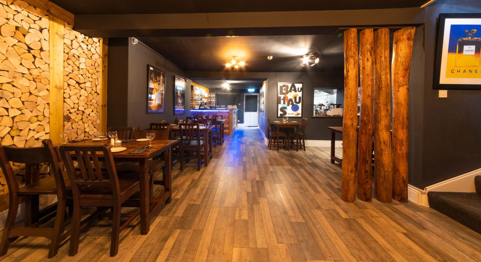 Long view through a restaurant dining room with a stacked log wall and timber floor, the Log Room at the Feversham Arms, Helmsley