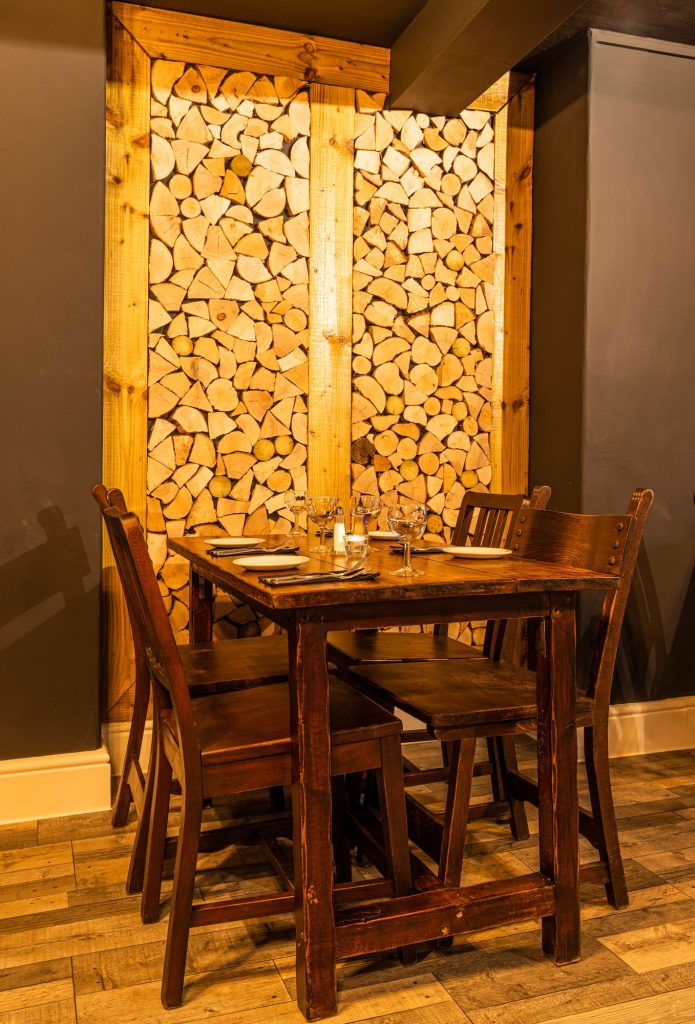 Dining table for four set against a stacked log-end feature wall, the Log Room at the Feversham Arms, Helmsley