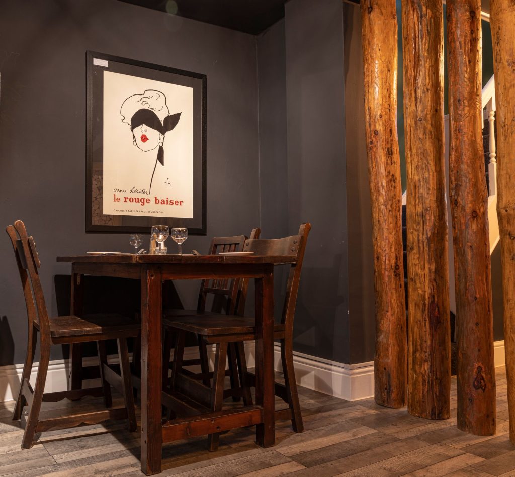 Restaurant table set for dinner beside reclaimed timber columns and a framed vintage poster, the Log Room at the Feversham Arms, Helmsley