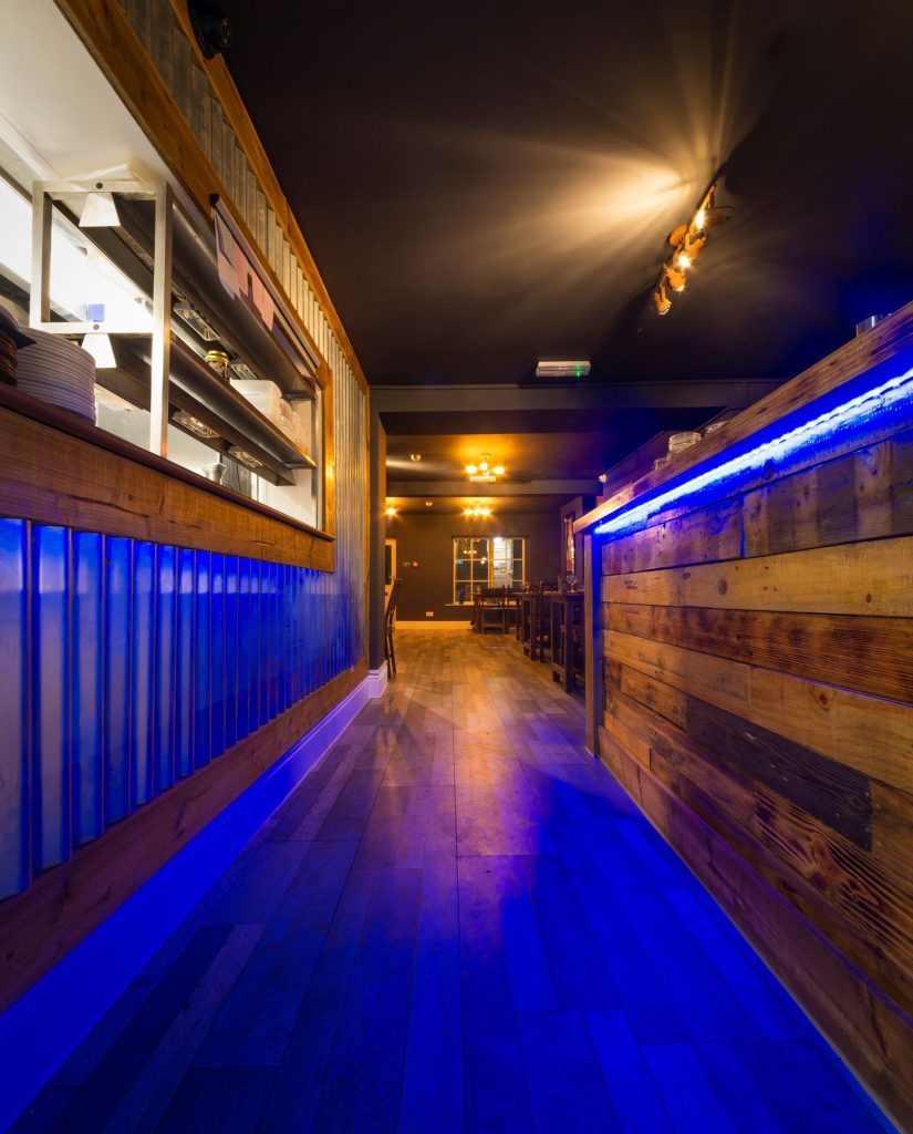 Narrow bar passage with timber cladding and blue LED strip lighting, the Log Room at the Feversham Arms, Helmsley